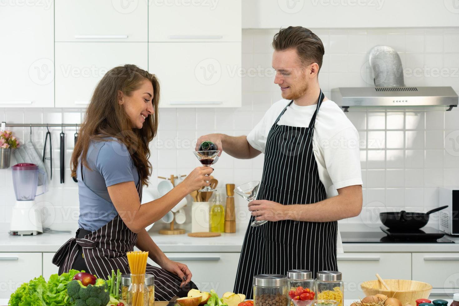 jong koppel wijn drinken tijdens het koken van voedsel foto