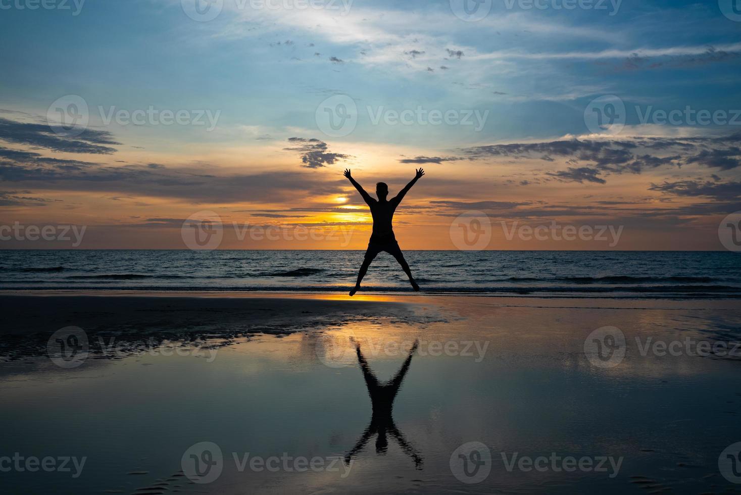 silhouet van de mens die op het strand springt bij zonsondergang foto