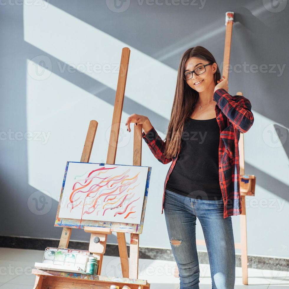 creatieve peinzende schilder meisje schildert een kleurrijke foto op canvas met olieverf in werkplaats.