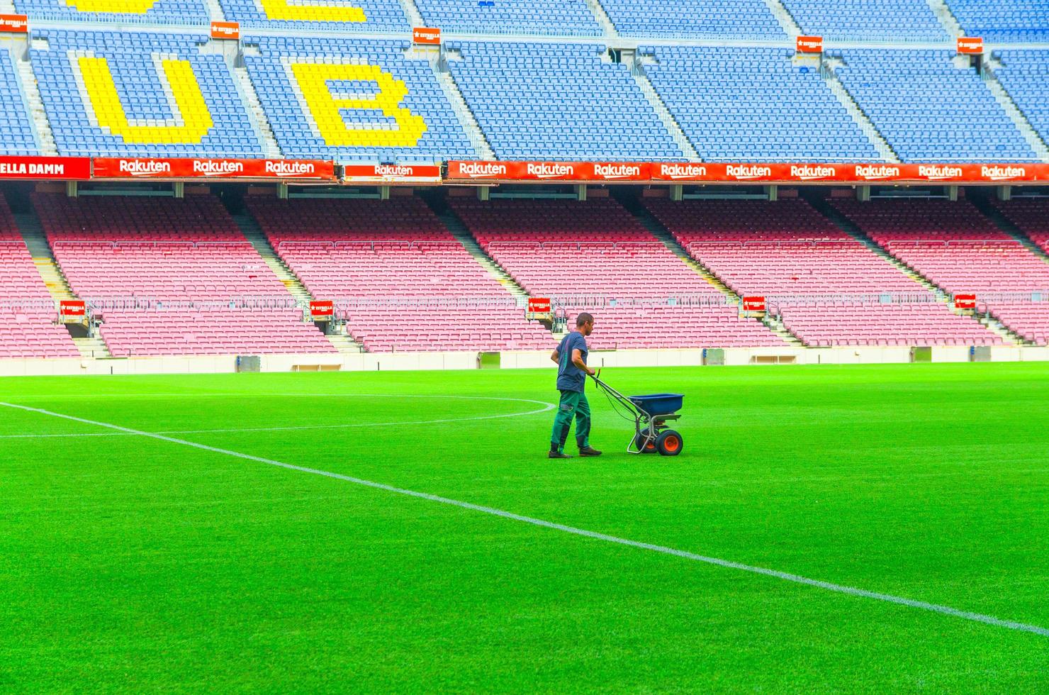 barcelona, spanje, 14 maart 2019 werknemer zaait gras met kunstmeststrooier op het gazon van camp nou green field, tribunes staat achtergrond. stadion van voetbalclub barcelona foto