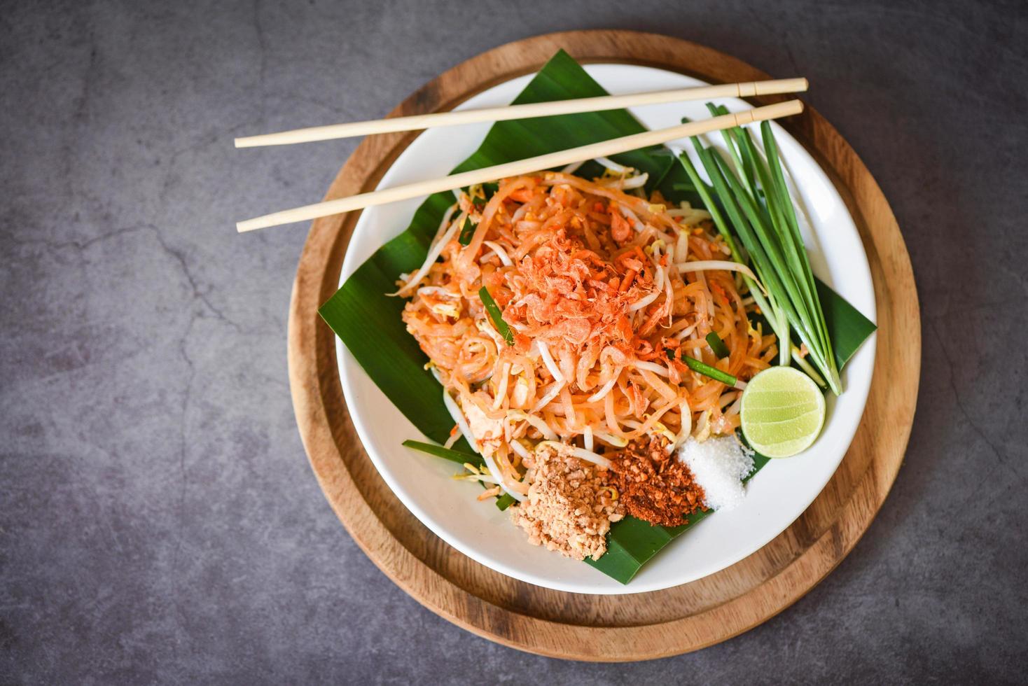 Thais eten gebakken noedels Thaise stijl met garnalen taugé en garnituur pinda's chili poeder suiker citroen limoen, roerbak noedels pad thai op bord geserveerd op de eettafel eten - bovenaanzicht foto