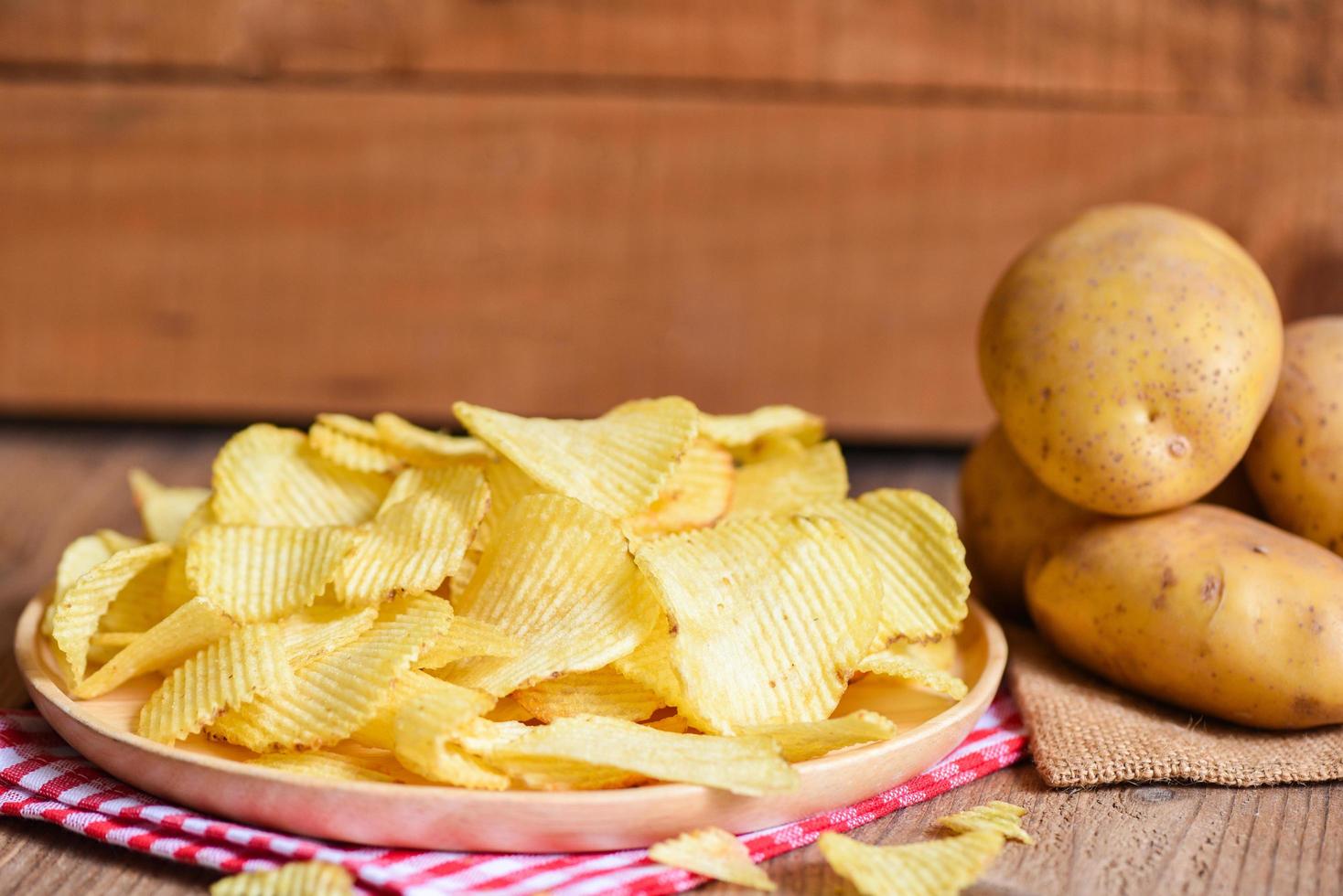 chips snack op wit bord, krokante chips op de keukentafel en verse rauwe aardappelen foto