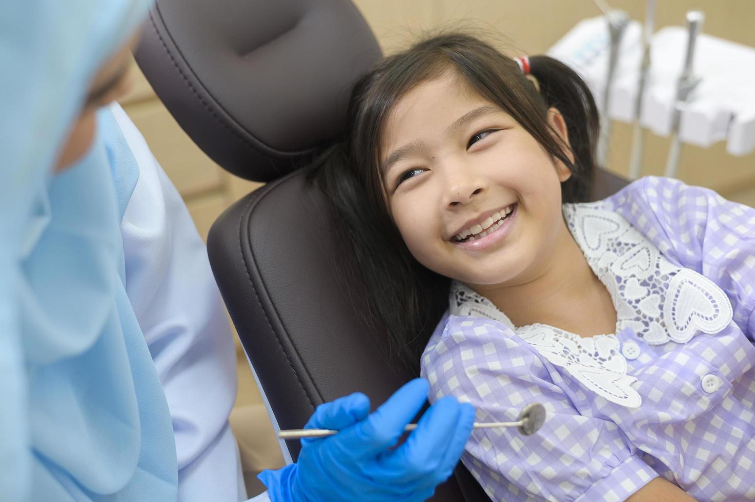 een klein schattig meisje met tanden onderzocht door moslim tandarts in tandheelkundige kliniek, tanden check-up en gezond gebit concept foto