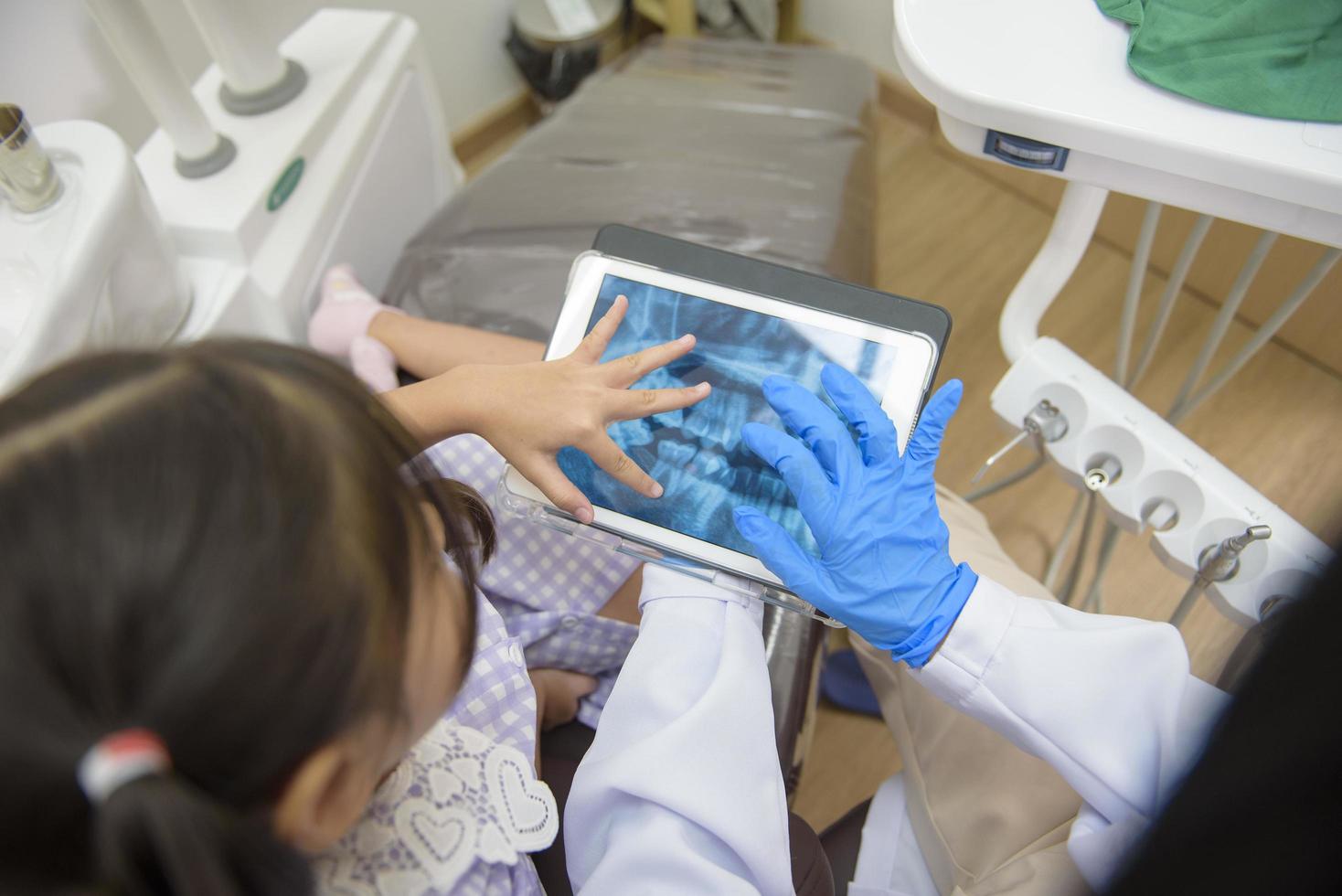 vrouwelijke tandarts die tandenröntgenfoto's uitlegt aan een klein meisje in de tandheelkundige kliniek, tandencontrole en gezond tandenconcept foto