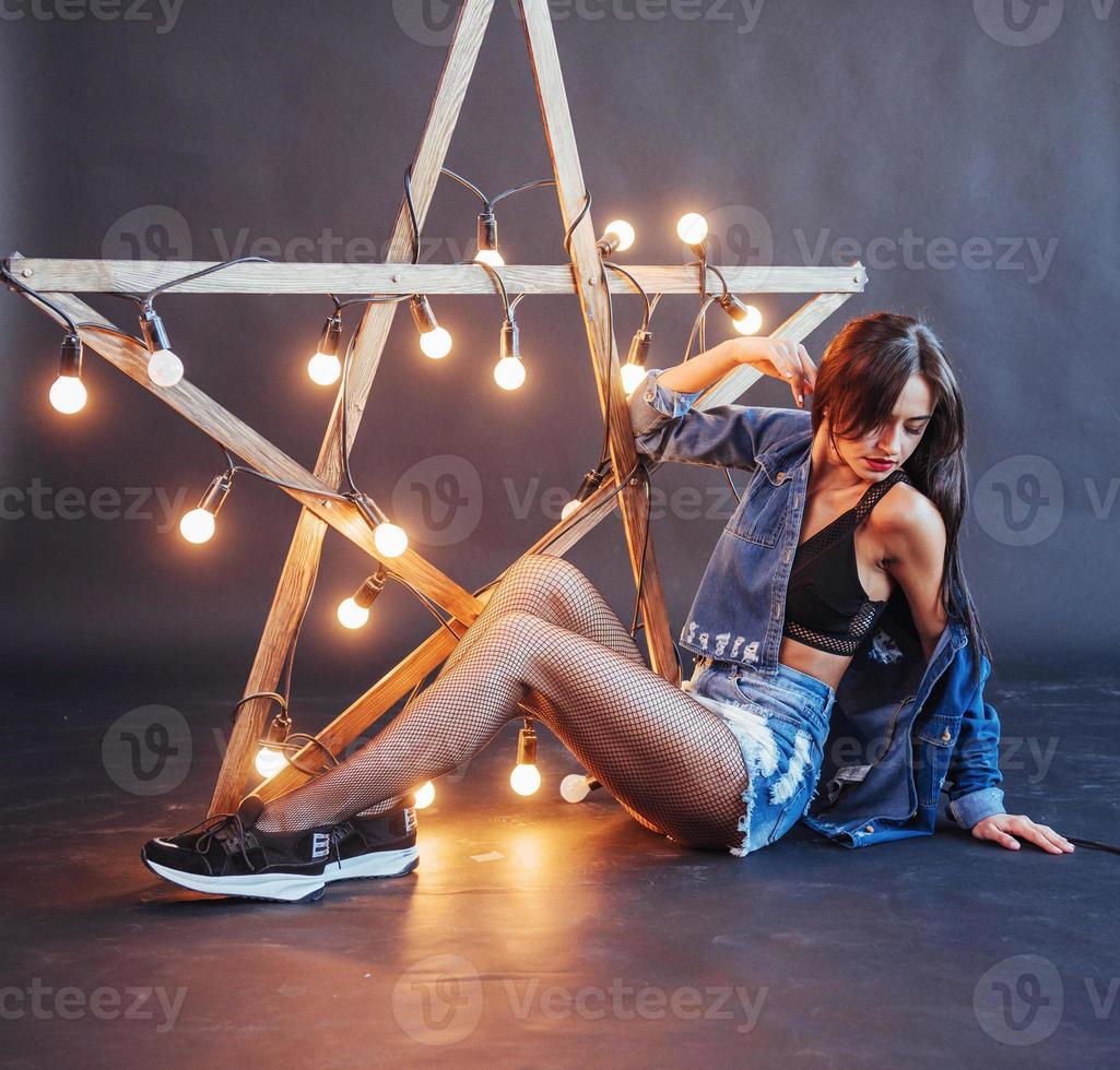 sexy brunette vrouw in mooie jeans in de studio. houten ster met lampjes op een zwarte achtergrond foto