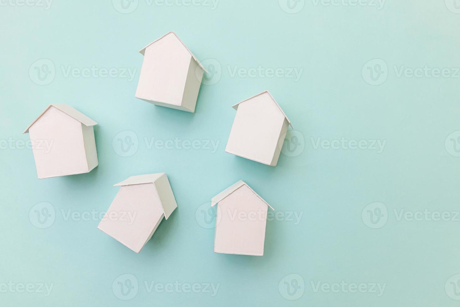 eenvoudig plat ontwerp met miniatuur witte speelgoedmodelhuizen geïsoleerd op pastelblauwe achtergrond. hypotheek onroerend goed verzekering droom huis concept. plat lag bovenaanzicht kopieerruimte. foto