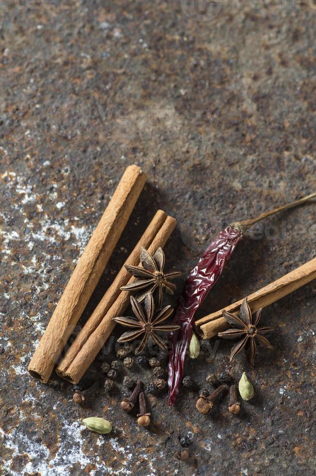 specerijen en kruiden. voedsel en keuken ingrediënten. kaneelstokjes, anijssterren, zwarte peperkorrels, chili, kardemom en kruidnagel op gestructureerde achtergrond foto