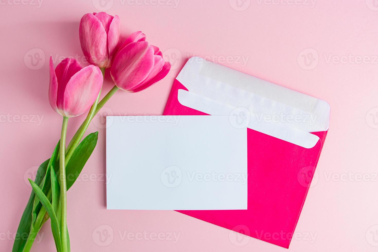 envelop met uitnodiging voor vakantie en boeket tulpen op roze achtergrond. foto