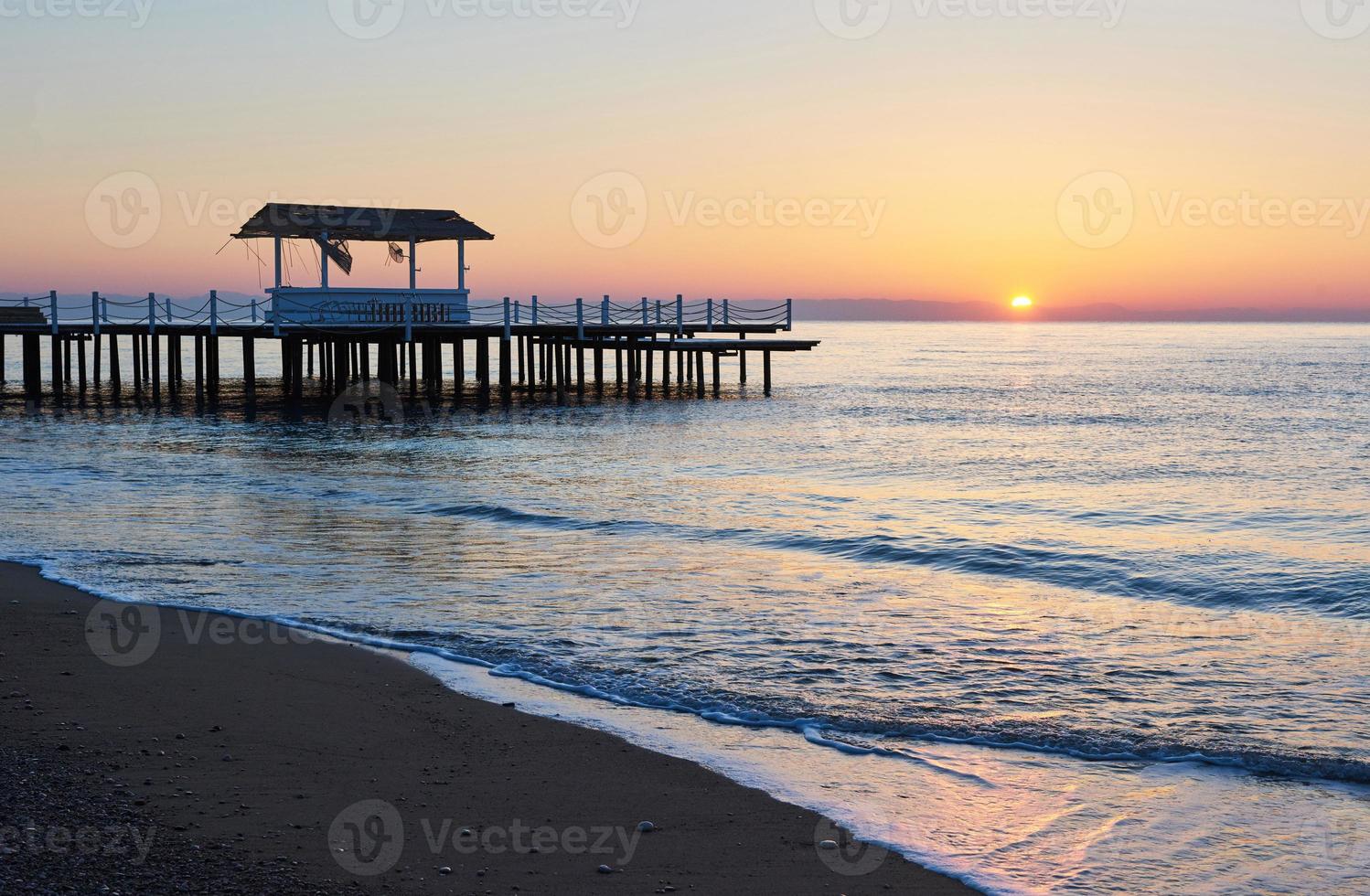 prieel op de houten pier de zee in met de zon bij zonsondergang foto