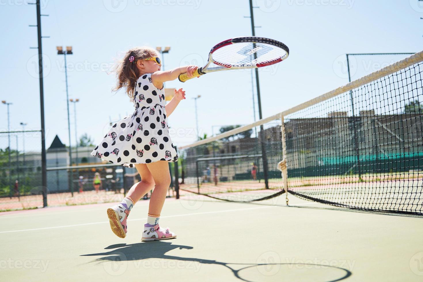 schattig klein meisje tennist buiten op de tennisbaan foto