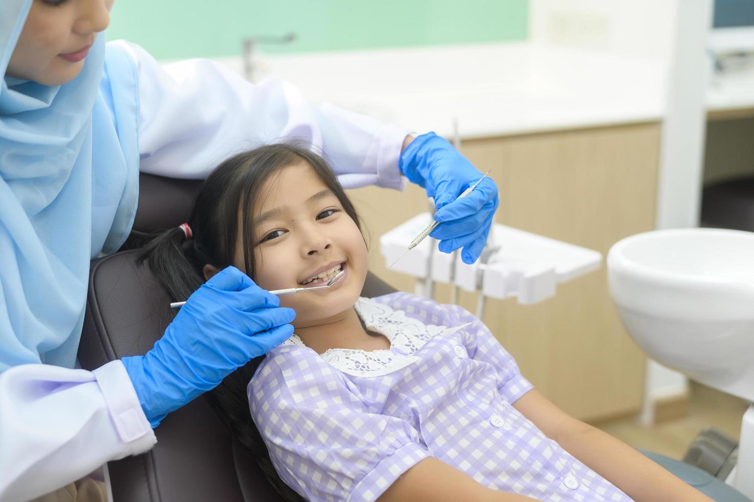 een klein schattig meisje met tanden onderzocht door moslim tandarts in tandheelkundige kliniek, tanden check-up en gezond gebit concept foto