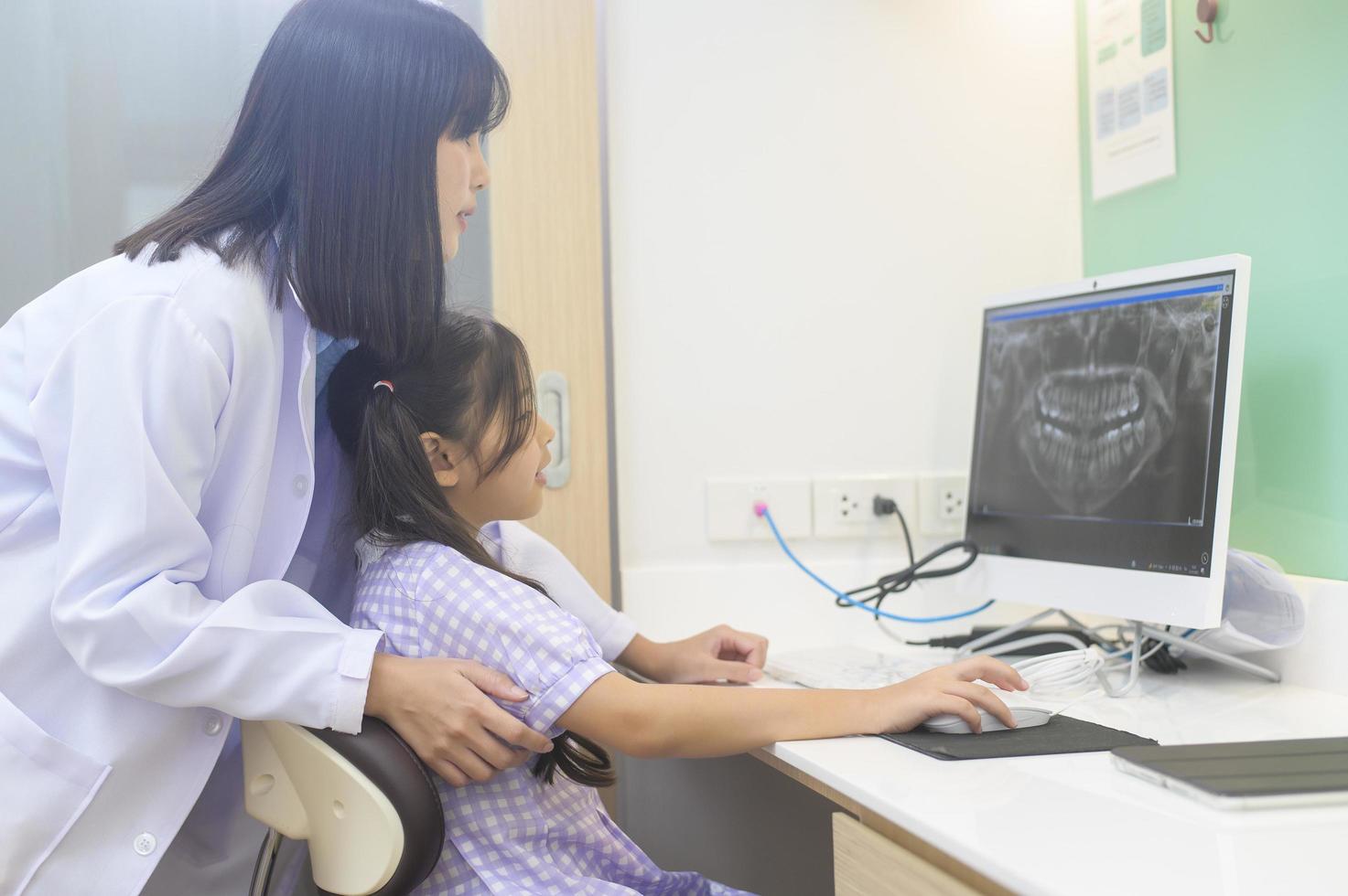 vrouwelijke tandarts die tandenröntgenfoto's uitlegt aan een klein meisje in de tandheelkundige kliniek, tandencontrole en gezond tandenconcept foto