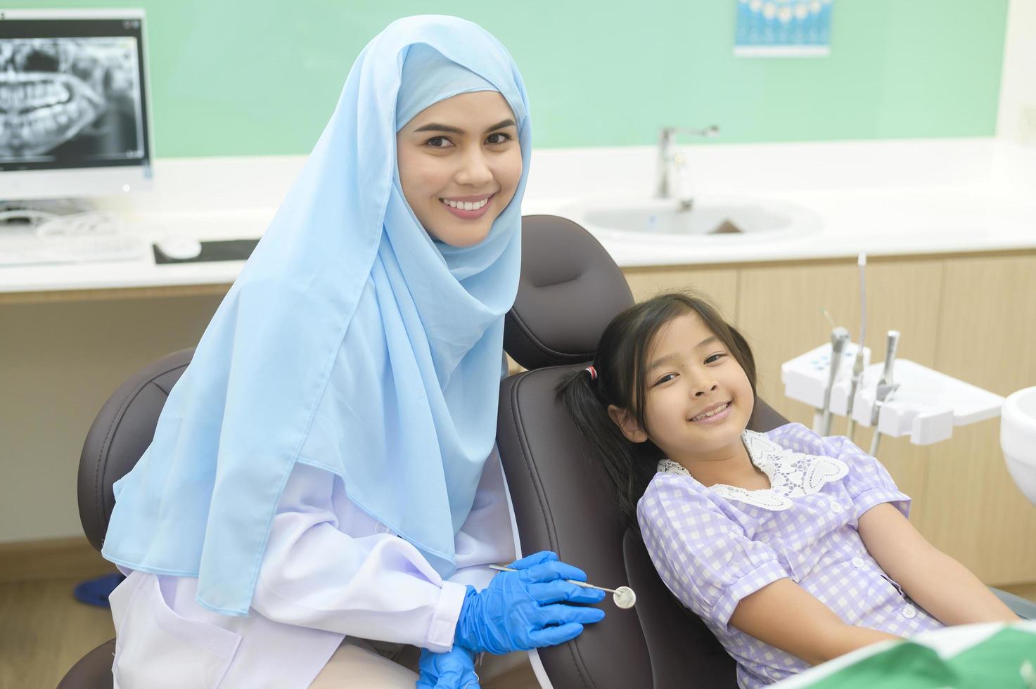 een klein schattig meisje met tanden onderzocht door moslim tandarts in tandheelkundige kliniek, tanden check-up en gezond gebit concept foto