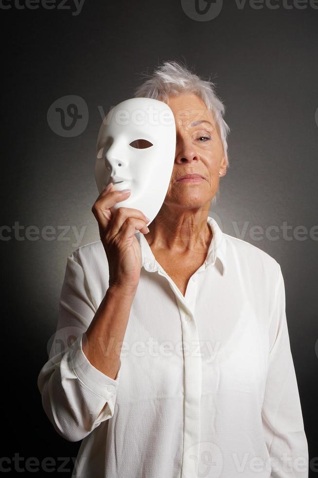 serieuze volwassen vrouw die gezicht achter masker onthult foto