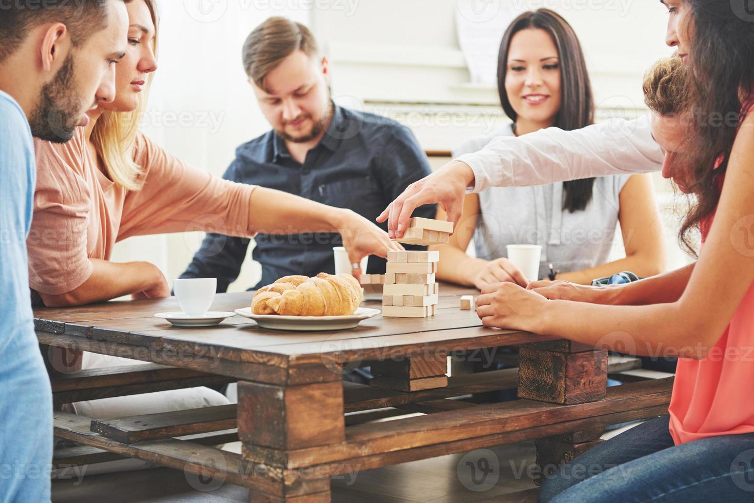 groep creatieve vrienden zitten aan houten tafel. mensen die plezier hebben tijdens het spelen van een bordspel foto