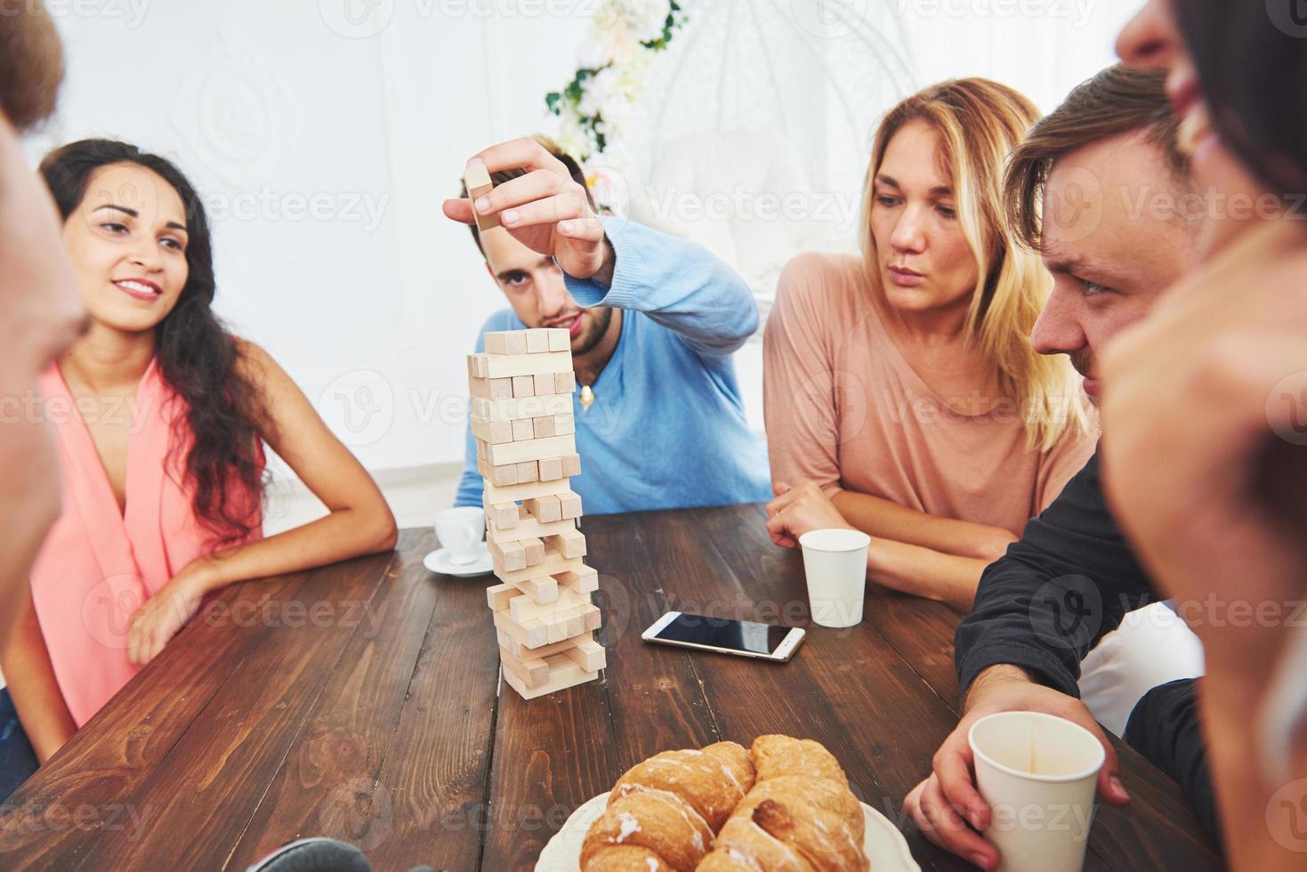 groep creatieve vrienden zitten aan houten tafel. mensen die plezier hebben tijdens het spelen van een bordspel foto