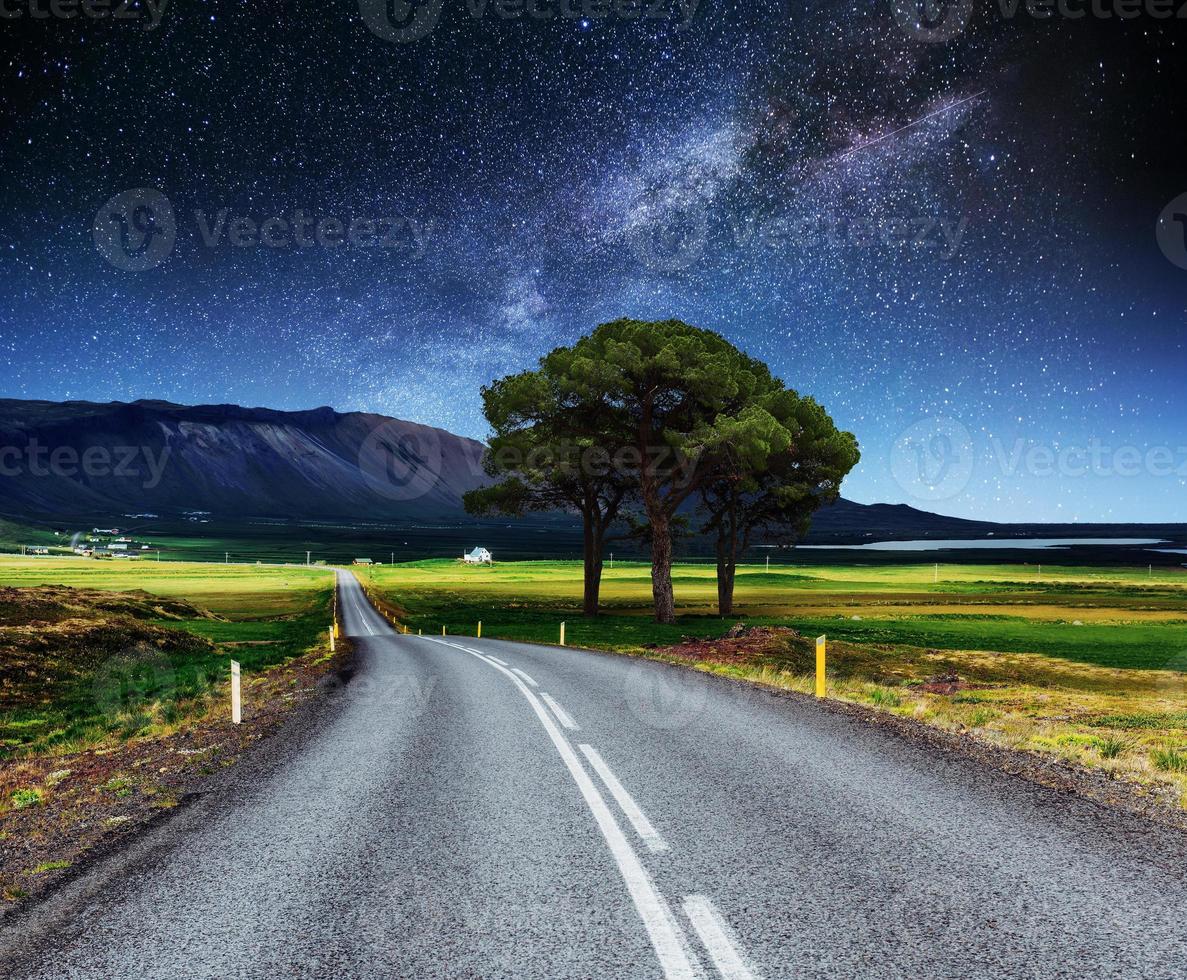 asfaltweg en eenzame boom onder een sterrenhemel en de melkweg foto