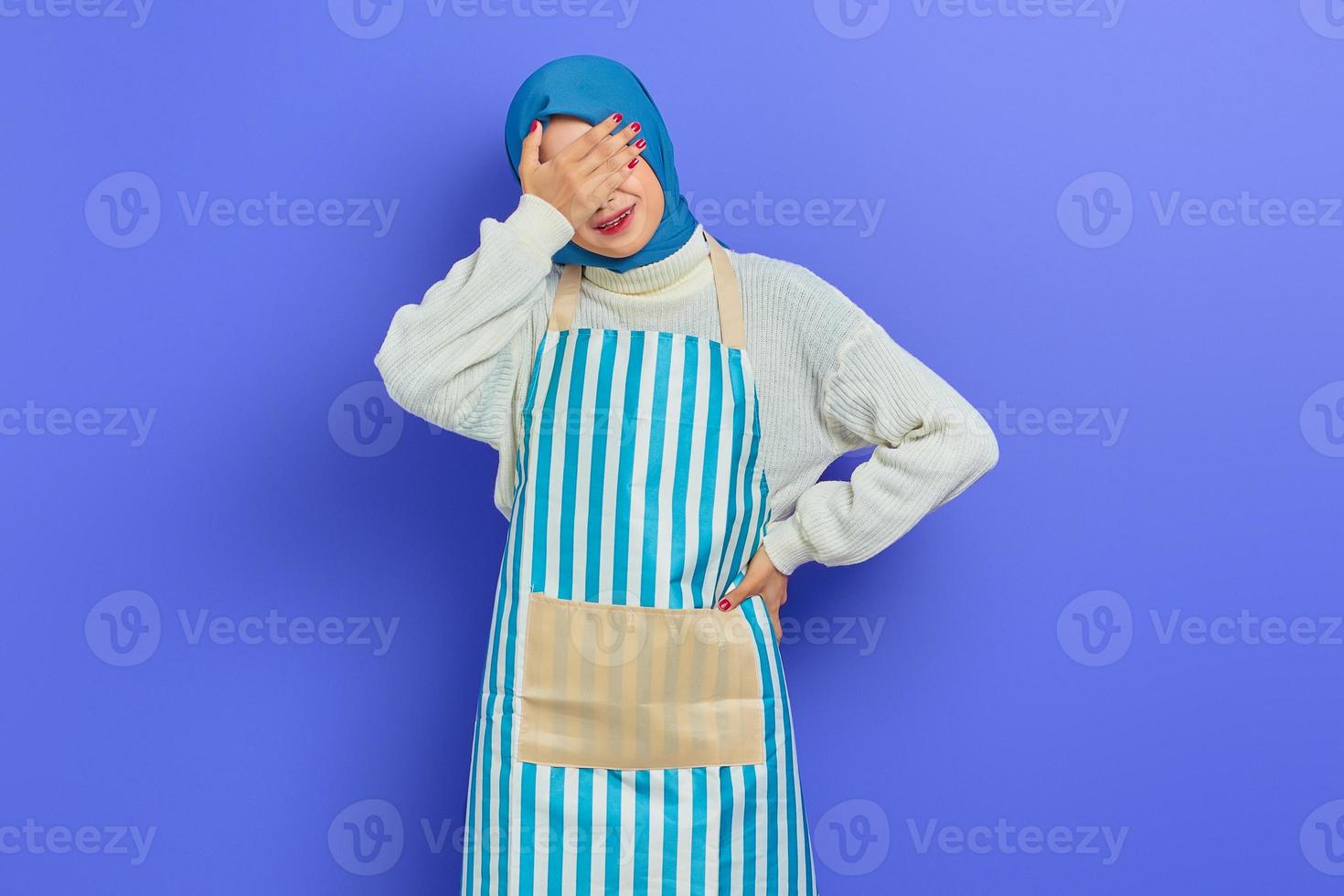 mooie jonge huisvrouw vrouw in hijab en stiped schort, die ogen bedekt met één hand bang of angstig geïsoleerd op paarse achtergrond. mensen huisvrouw moslim lifestyle concept foto