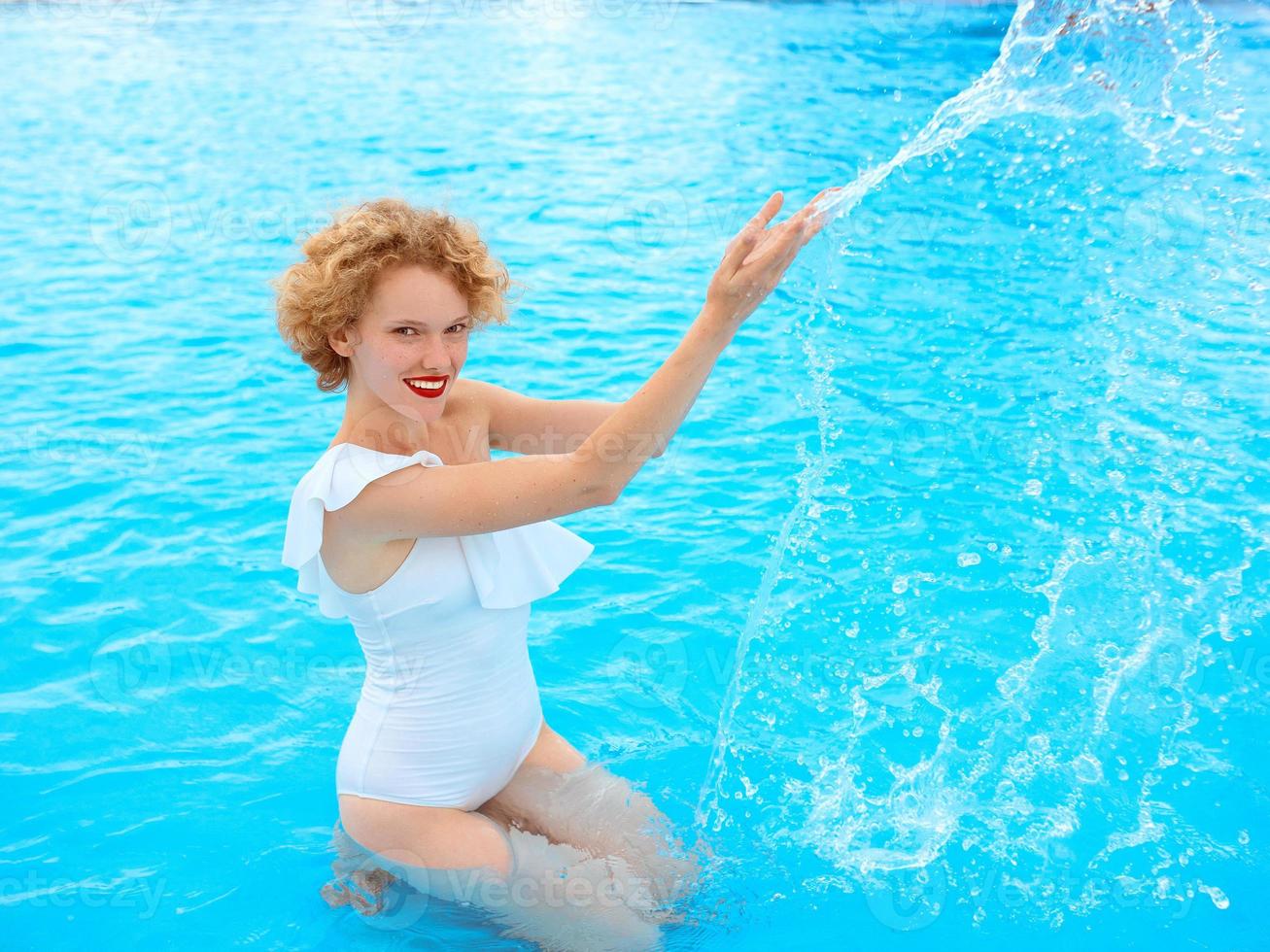 glimlachend roodharige vrouw portret genietend van het leven in een wit zwempak in het zwembad foto