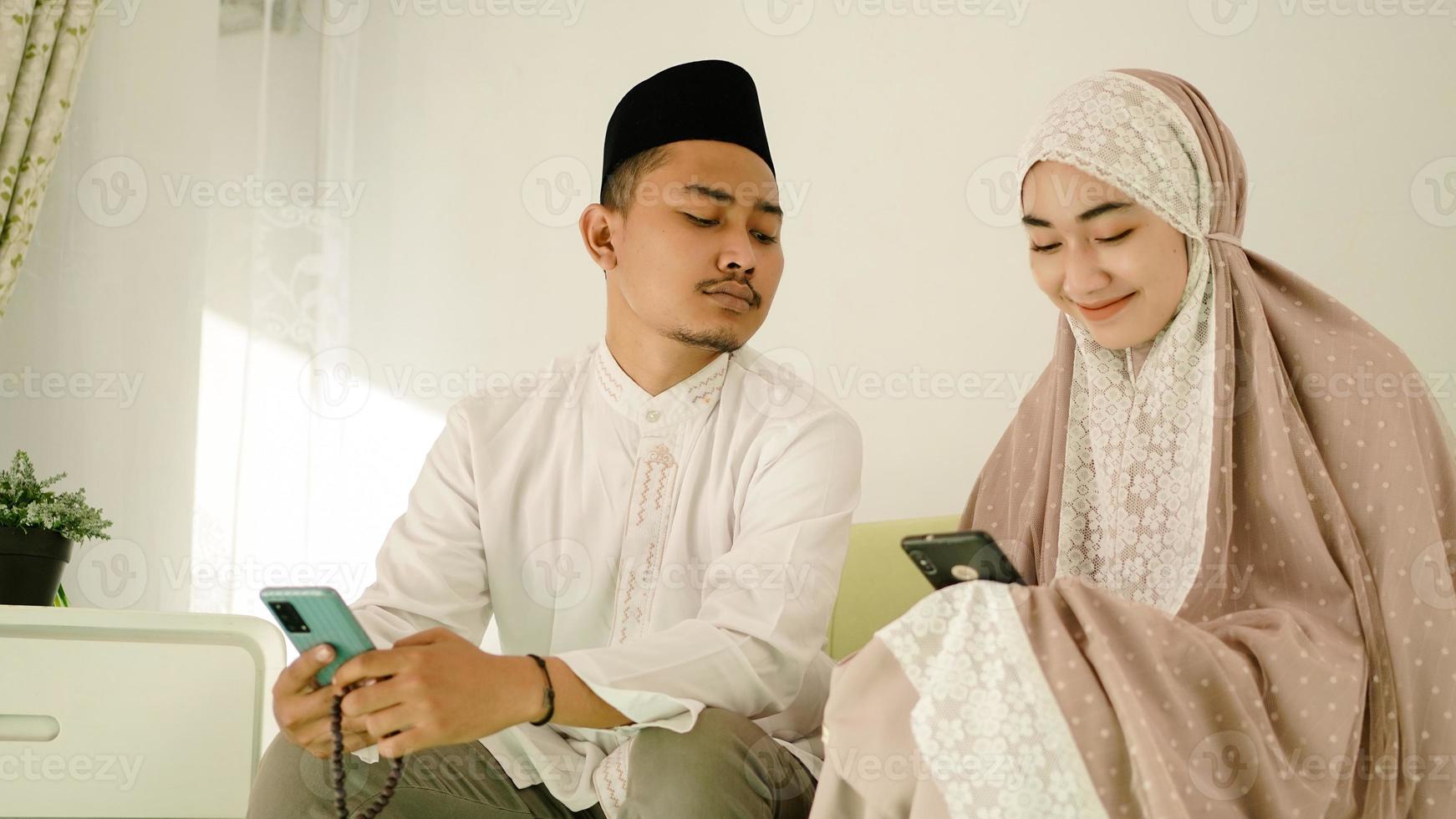 Aziatisch moslimpaar dat mobiele telefoon op de bank speelt foto