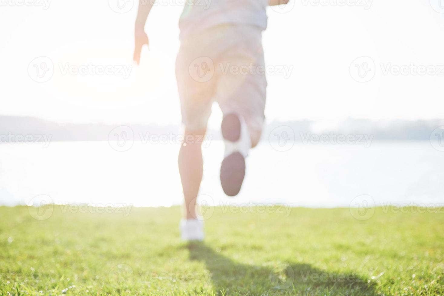buiten langlaufen in zomerzonconcept voor sporten, fitness en een gezonde levensstijl. close-up van de voeten van een man die in het gras rent foto