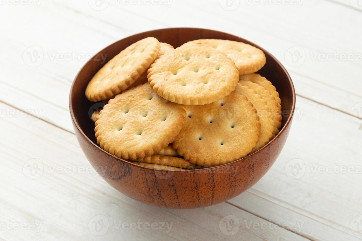 afgeronde crackerkoekjes in een houten kom op witte houten tafelachtergrond foto