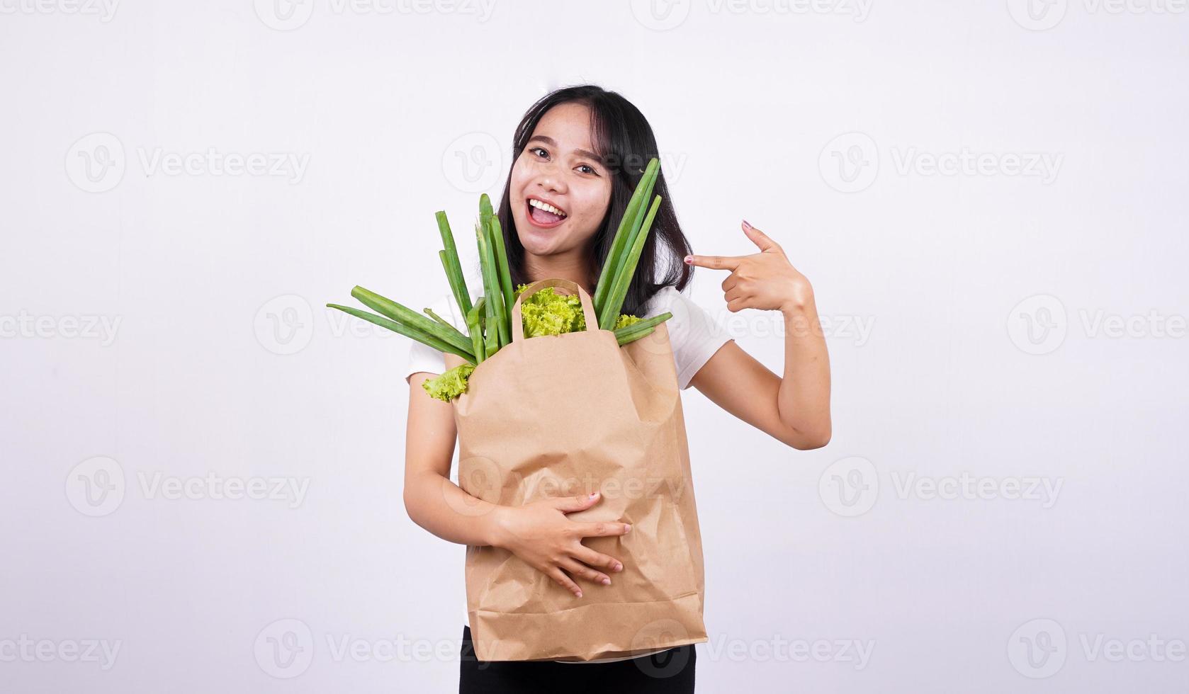 mooie aziatische vrouw die lacht met papieren zak verse groenten met geïsoleerde witte achtergrond foto
