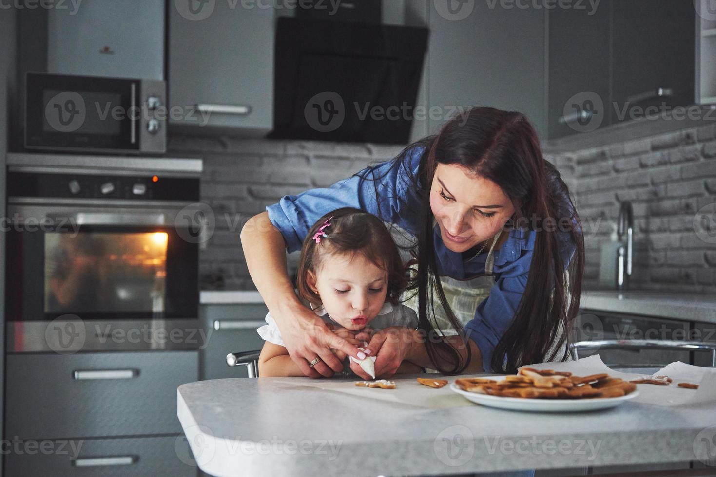 gelukkige familie in de keuken. vakantie voedsel concept. moeder en dochter versieren koekjes. gelukkige familie bij het maken van zelfgemaakt gebak. zelfgemaakt eten en kleine helper foto