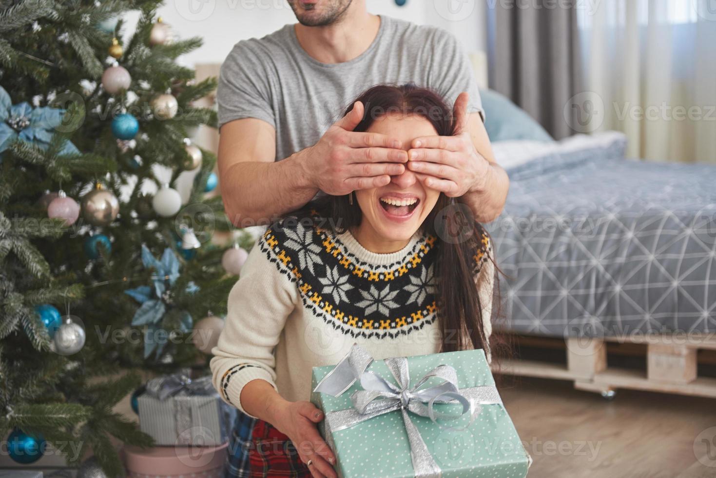 jong koppel kerst vieren. een man gaf plotseling een cadeau aan zijn vrouw. het concept van gezinsgeluk en welzijn foto