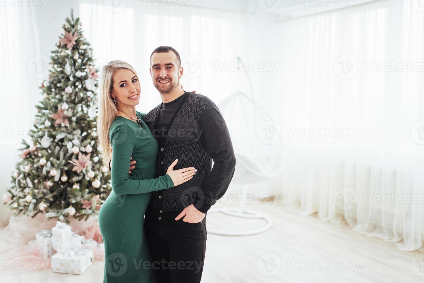 gelukkig jong stel met kerstmis, mooie cadeaus en boom op de achtergrond foto