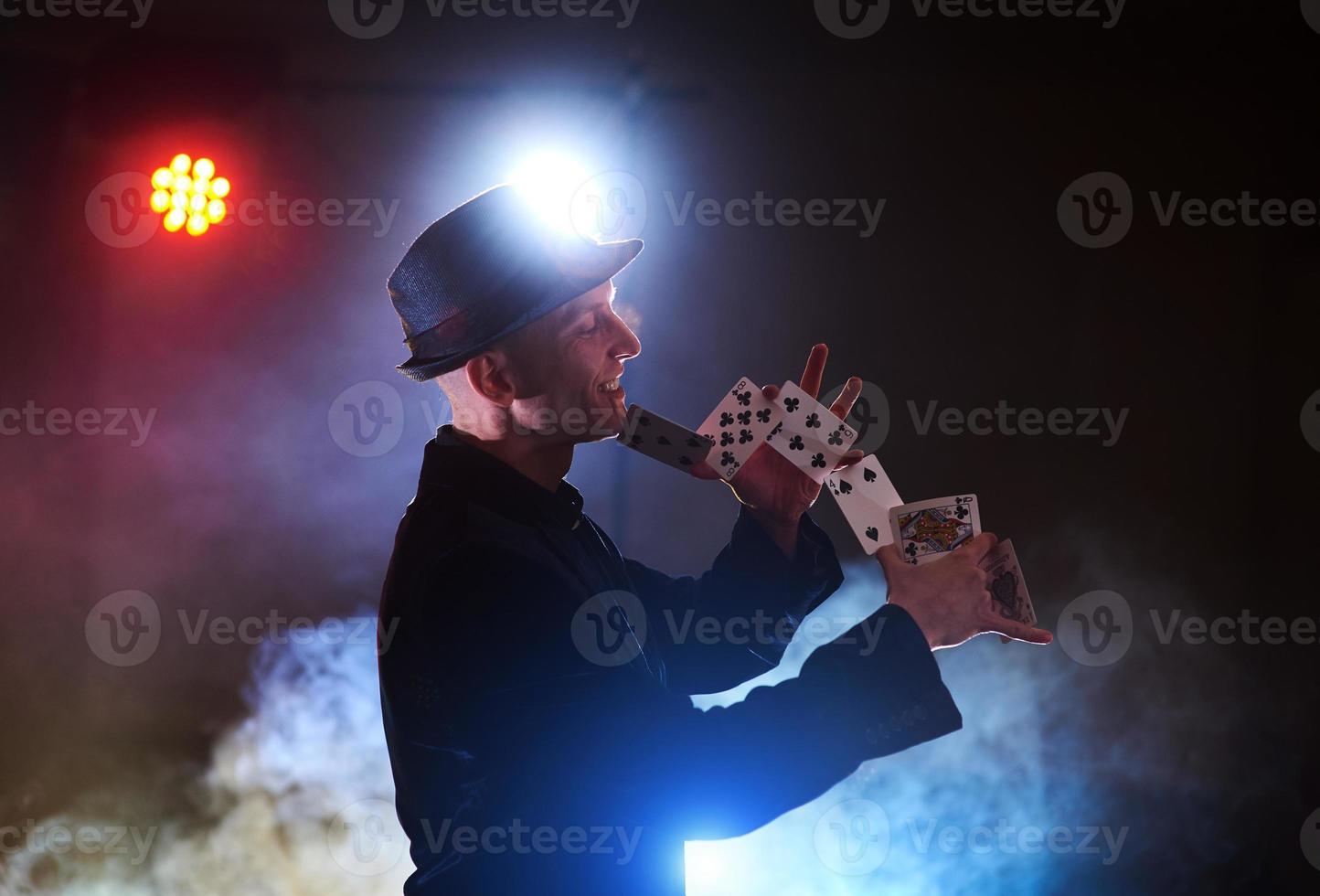 goochelaar die truc met speelkaarten toont. magie of behendigheid, circus, gokken. prestidigitator in donkere kamer met mist foto