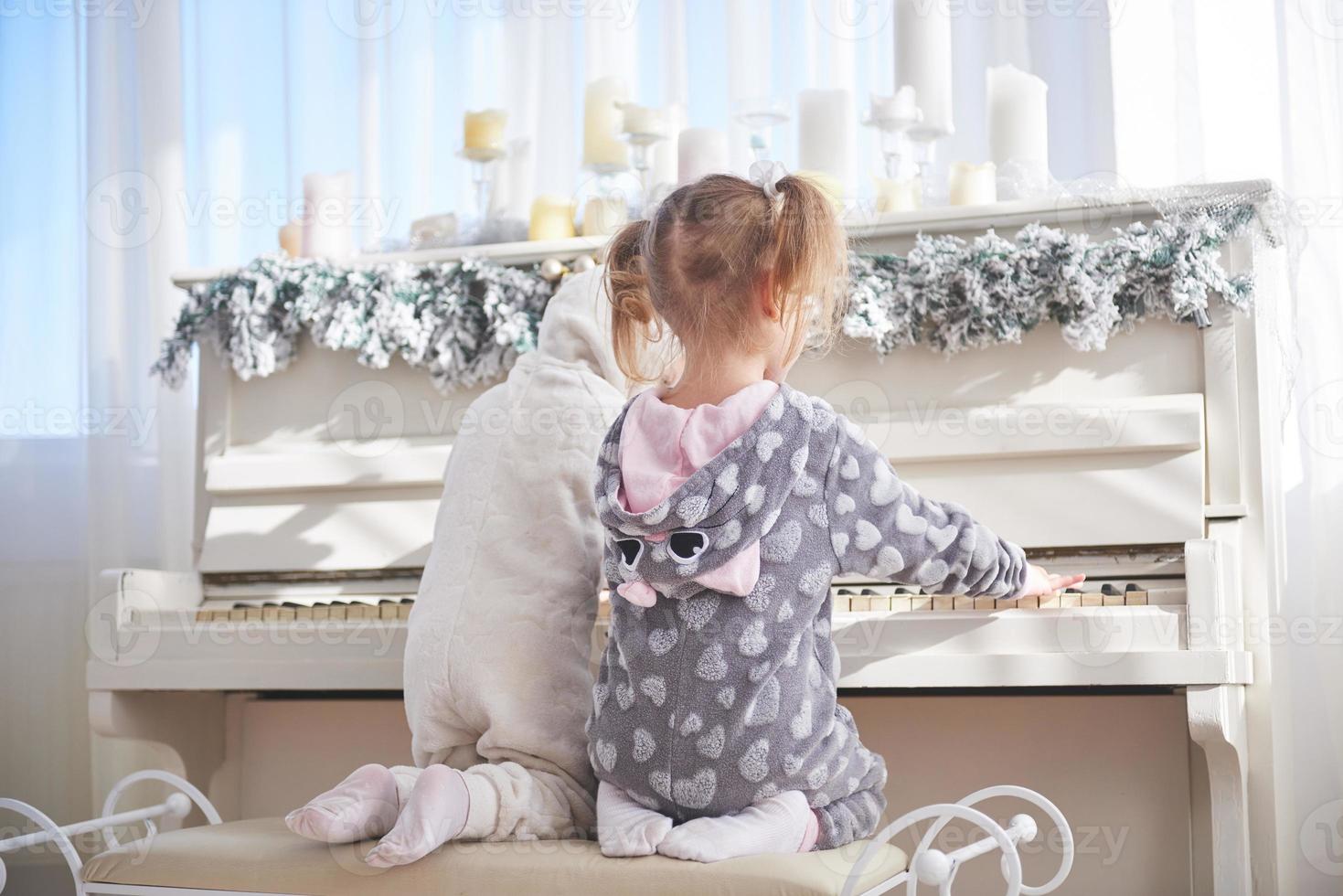 twee gelukkige kleine meisjes in pyjama spelen piano op eerste kerstdag foto