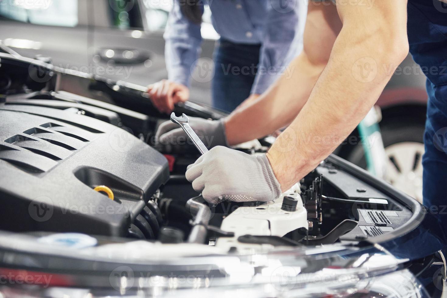 een man-monteur en een vrouwelijke klant kijken naar de motorkap en bespreken reparaties foto