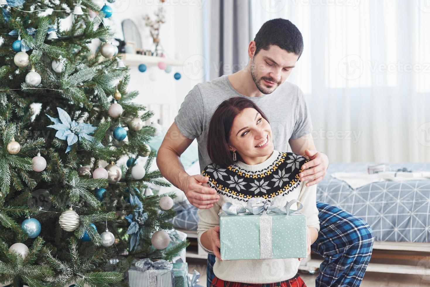 jong koppel kerst vieren. een man gaf plotseling een cadeau aan zijn vrouw. het concept van gezinsgeluk en welzijn foto