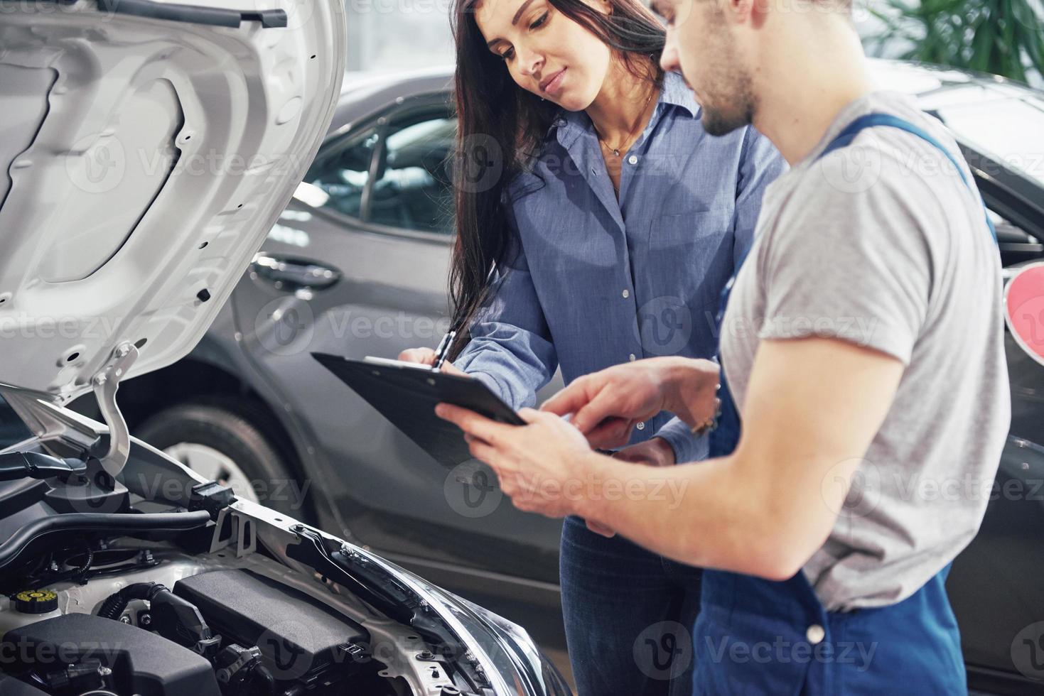 een mannelijke monteur en een vrouwelijke klant die reparaties aan haar voertuig bespreken foto