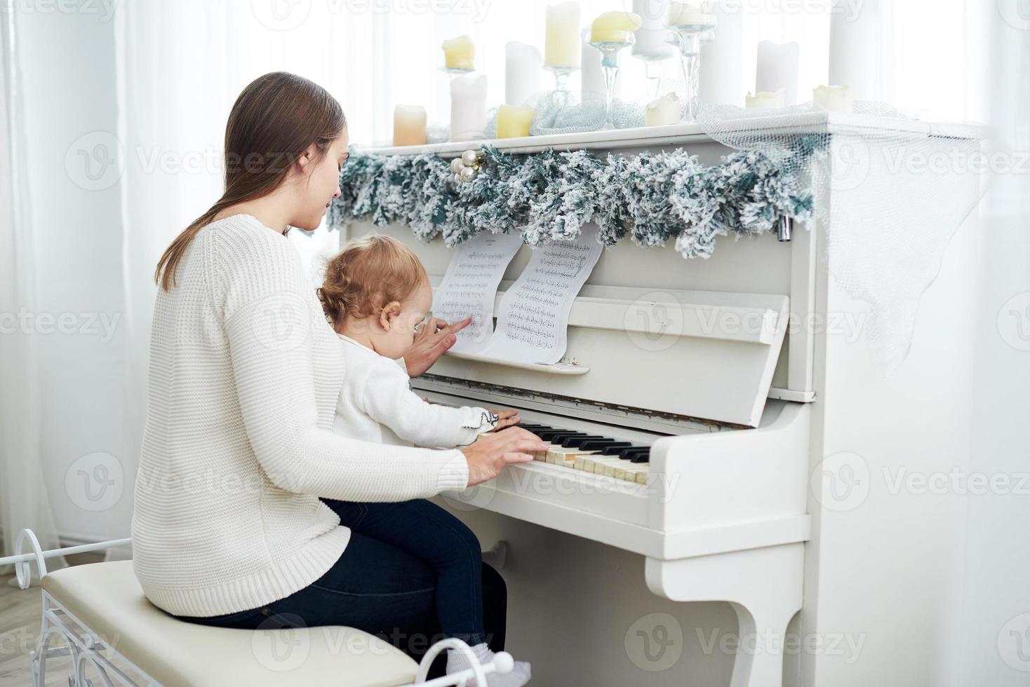 kijk van achteren naar moeder en dochter die witte piano spelen foto