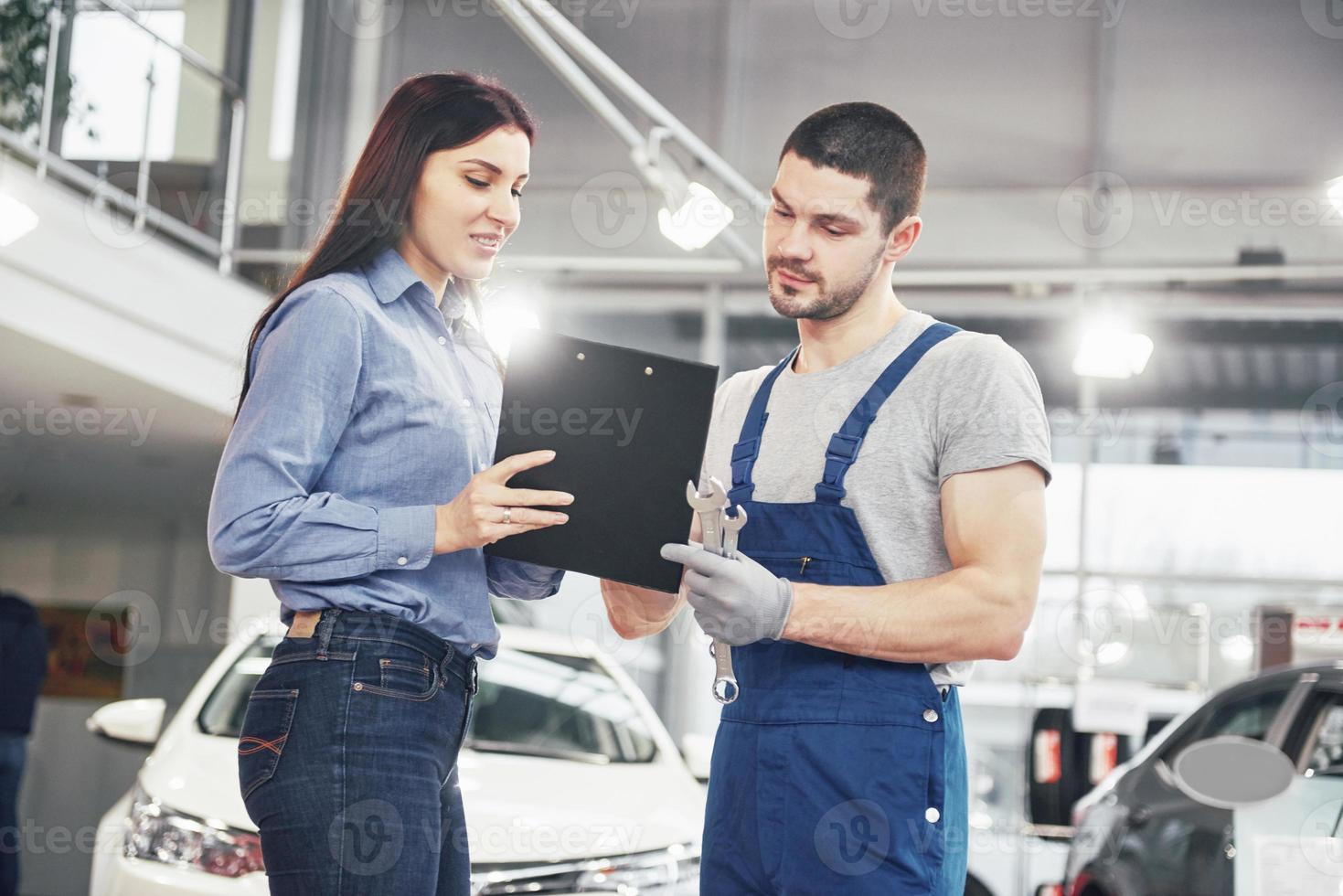 een mannelijke monteur en een vrouwelijke klant die reparaties aan haar voertuig bespreken foto