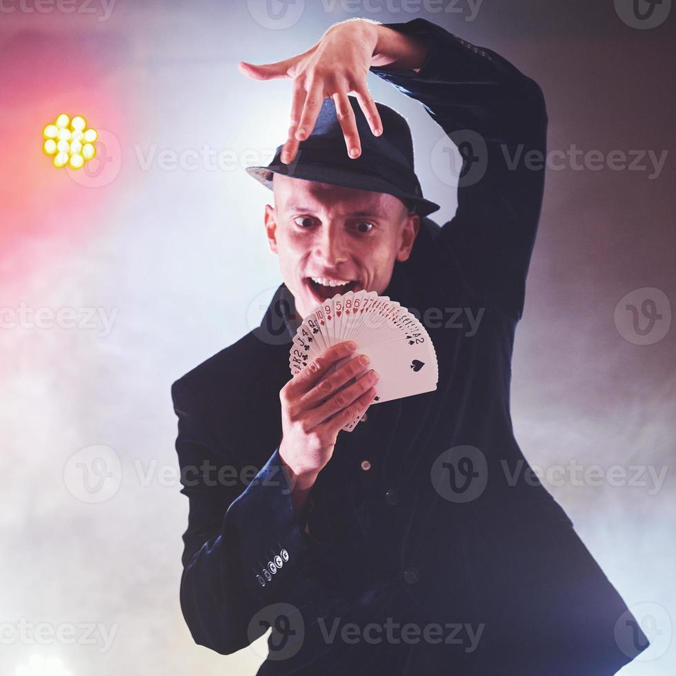 goochelaar die truc met speelkaarten toont. magie of behendigheid, circus, gokken. prestidigitator in donkere kamer met mist foto