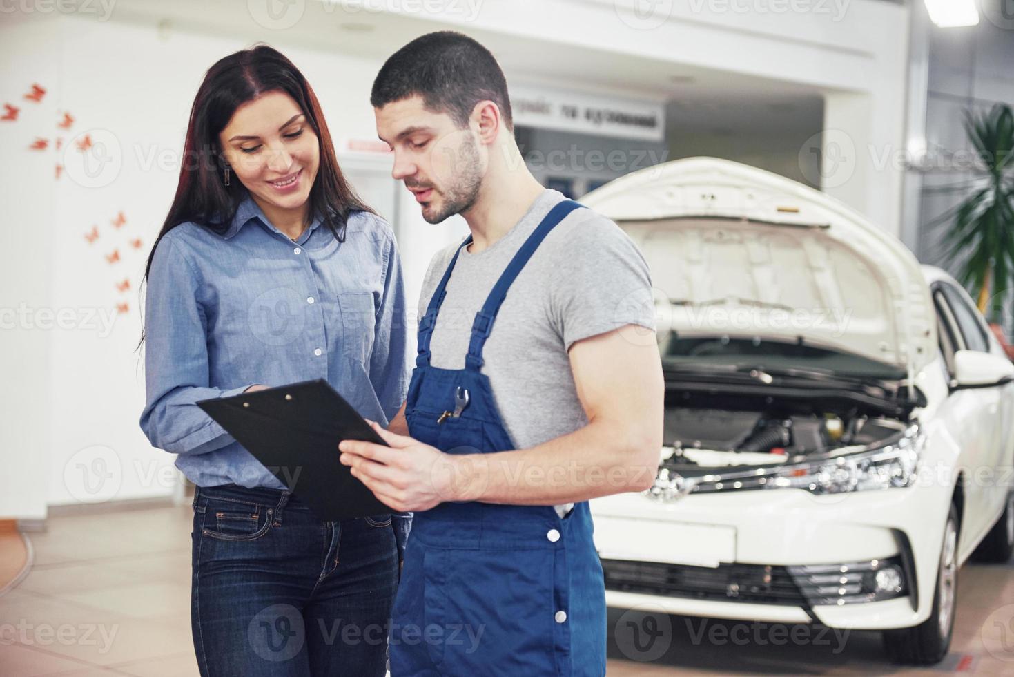 een mannelijke monteur en een vrouwelijke klant die reparaties aan haar voertuig bespreken foto