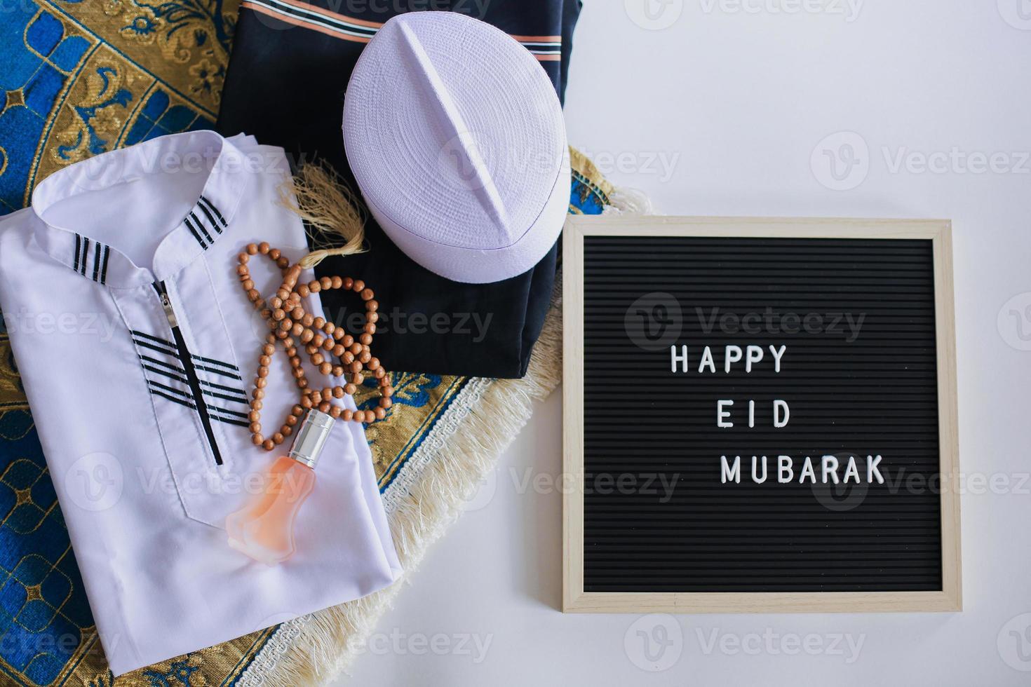 bovenaanzicht van moslim traditionele kleding en gebedskralen op de gebedsmat met letterbord zegt happy eid mubarak foto