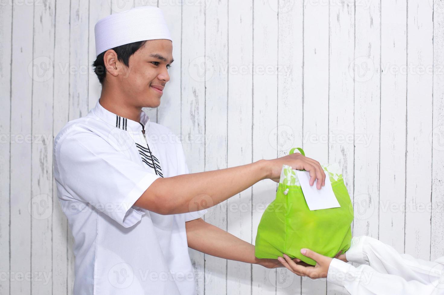 religieuze moslimman die aalmoezen geeft in de vorm van voedsel in een groene zak en een witte envelop gevuld met geld foto