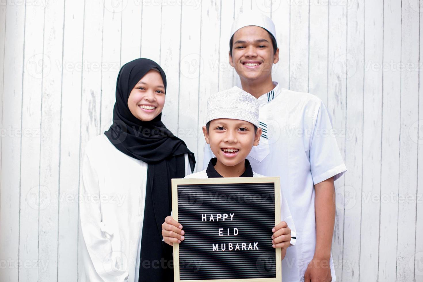 jonge aziatische moslimfamilie die traditionele kleding draagt en de jongen met een letterbord zegt happy eid mubarak foto