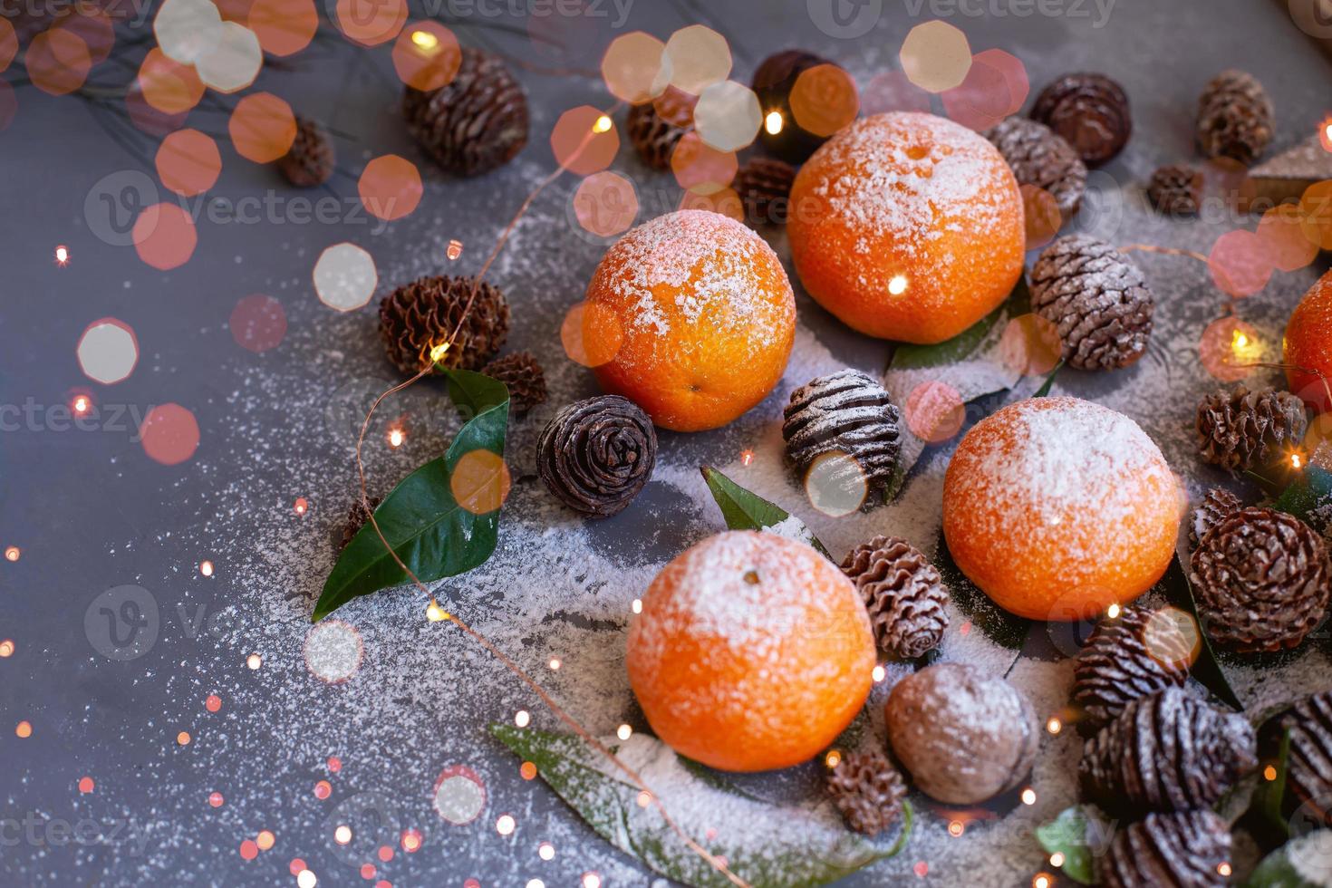 oranje mandarijnen op grijze achtergrond in nieuwjaarsdecor met bruine dennenappels en groene bladeren. kerstversiering met mandarijnen. heerlijke zoete clementine. foto