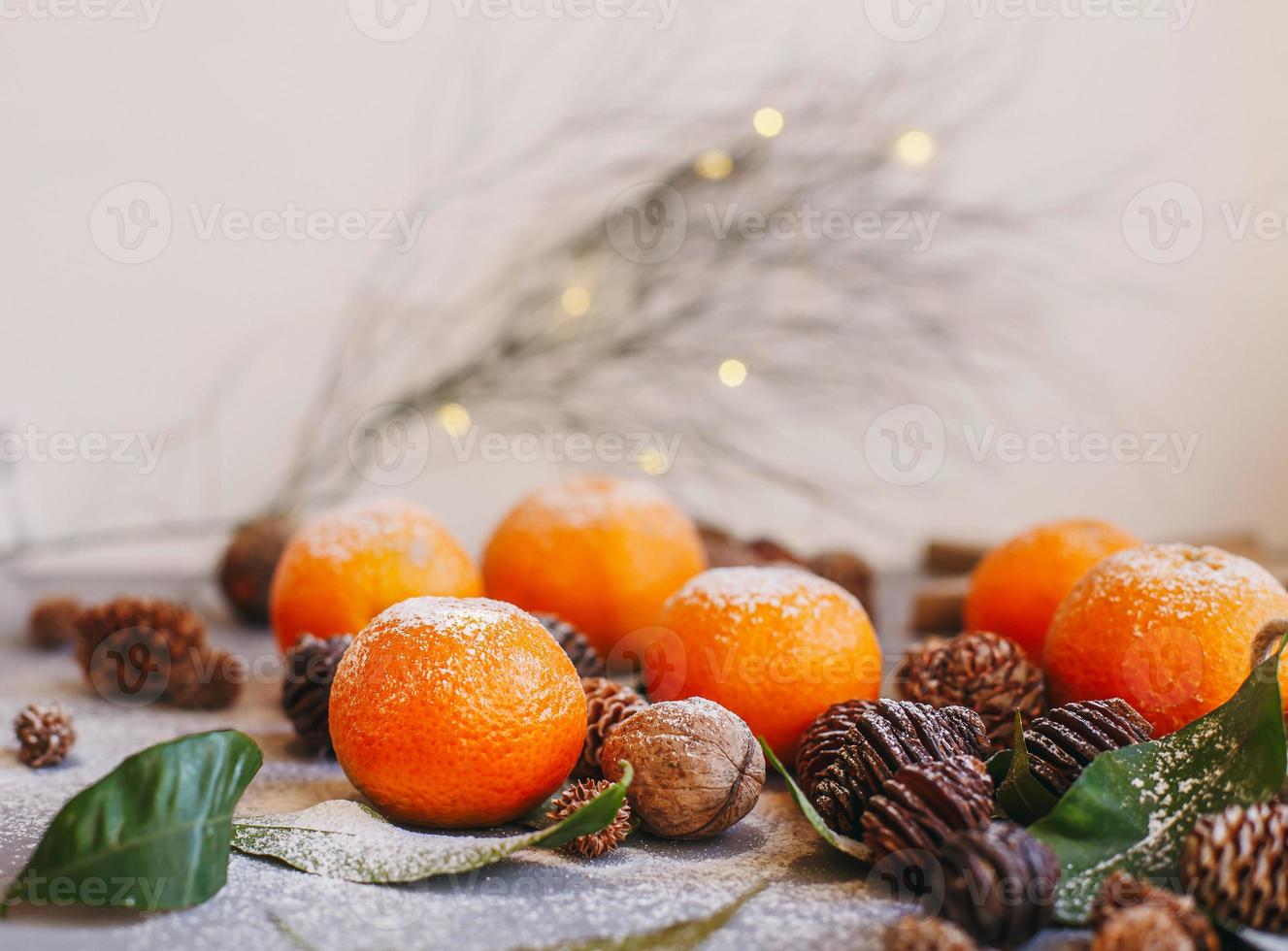 oranje mandarijnen op grijze achtergrond in nieuwjaarsdecor met bruine dennenappels en groene bladeren. kerstversiering met mandarijnen. heerlijke zoete clementine. foto