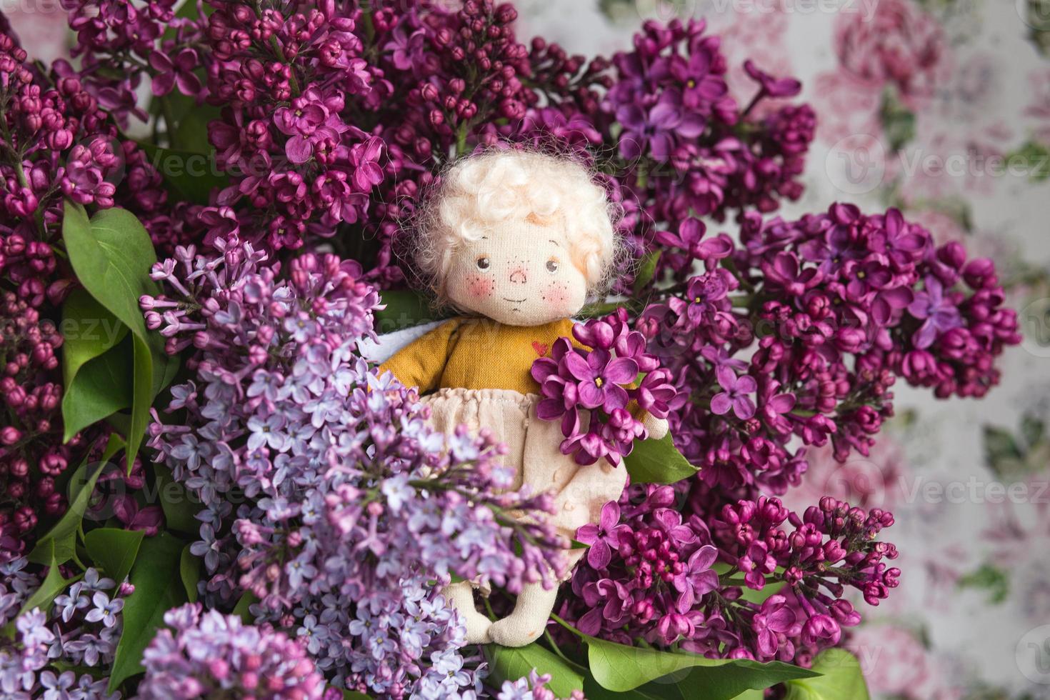 kleine goudharige engel in de blauwe, roze, paarse, violet lila bloemen. handgemaakt speelgoed in violet lila kleuren. wenskaart. foto