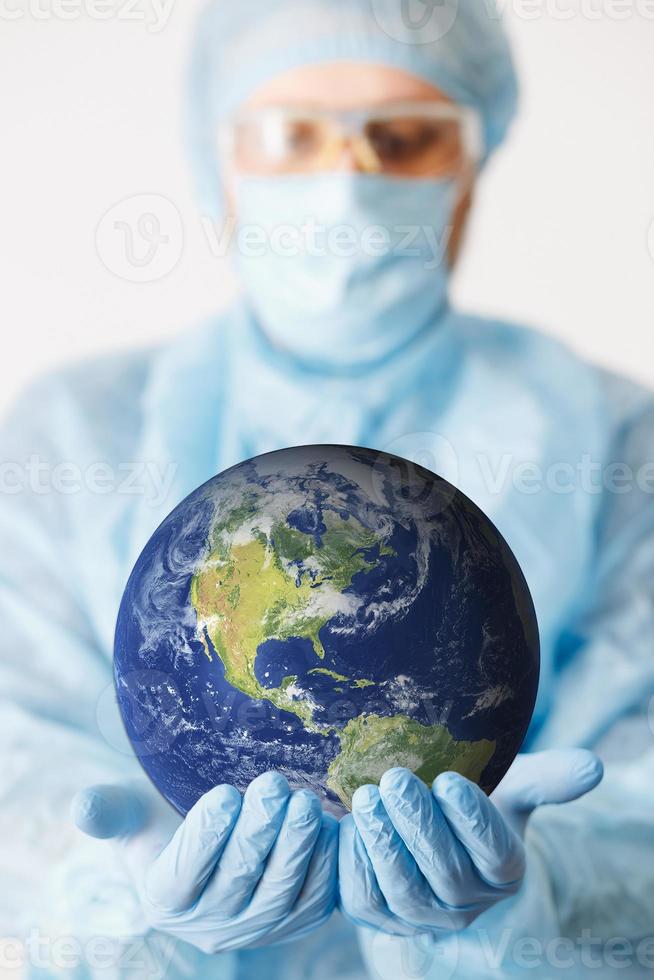 close-up van de hand van de arts die aarde vasthoudt. spotten. medische uitrusting. een arts die persoonlijke beschermingsmiddelen draagt, waaronder een masker, een veiligheidsbril en een pak om de covid-19-coronavirusinfectie te beschermen. foto