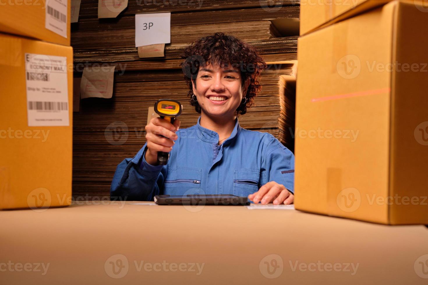 een vrouwelijke werknemer in veiligheidsuniform gebruikt een streepjescodescanner en tablet om verzendorders te controleren in het pakketmagazijn, papierfabriek voor de verpakkingsindustrie, logistieke transportservice. foto