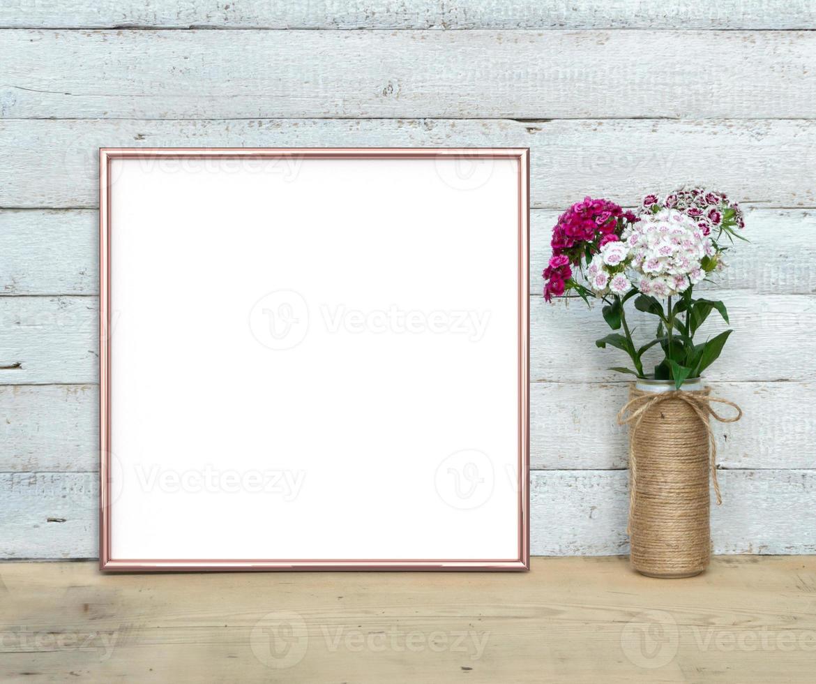 rose gouden vierkante frame mockup in de buurt van een boeket van zoete william staat op een houten tafel op een geschilderde witte houten achtergrond. rustieke stijl, eenvoudige schoonheid. 3D render. foto