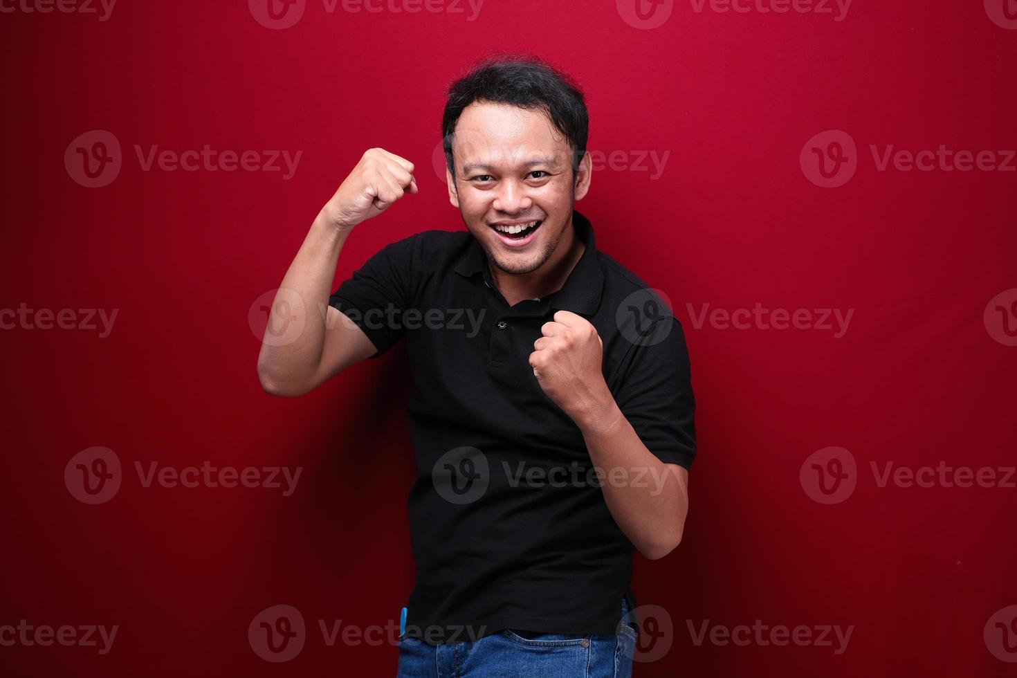 blij opgewonden en glimlachende jonge aziatische man die zijn arm opsteekt om succes of prestatie te vieren. foto