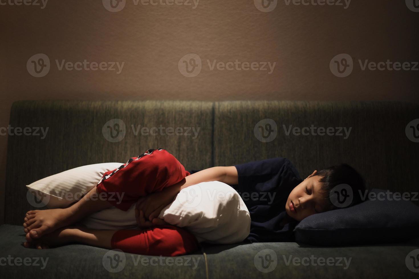 Aziatische jongen slaapt op de bank terwijl hij een kussen knuffelt foto